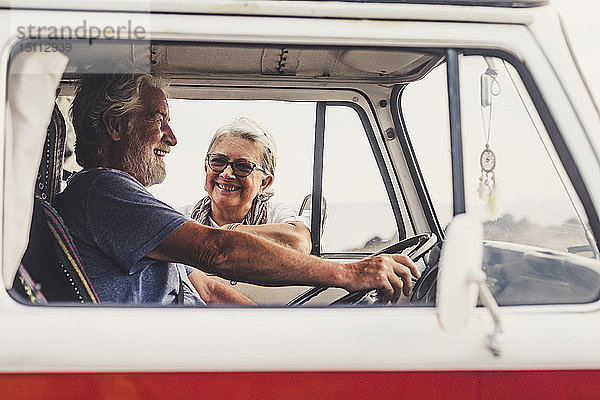 Älteres Ehepaar reist in einem Oldtimer-Van  macht eine Pause am Meer  unterhält