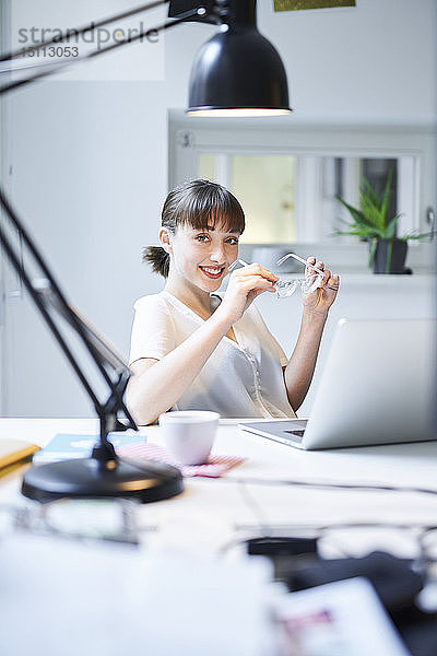 Porträt einer lächelnden jungen Geschäftsfrau  die am Schreibtisch in einem Büro sitzt