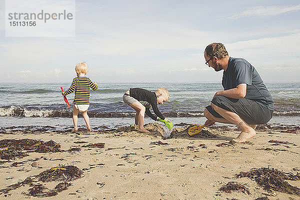 Vater mit zwei Kindern  die am Strand spielen