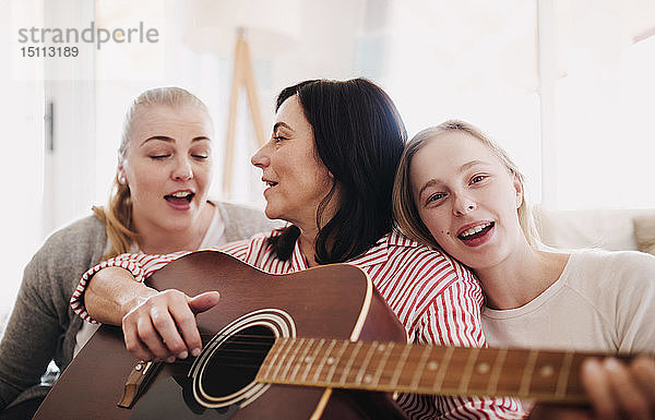 Reife Frau mit zwei Töchtern  die zu Hause singen und Gitarre spielen