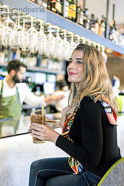 Lächelnde Frau mit einem Cocktail  die an der Theke einer Bar sitzt