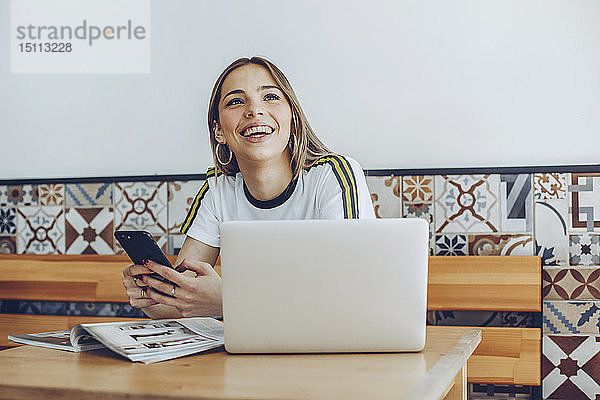 Junge Frau benutzt das Mobiltelefon und den Laptop im Café