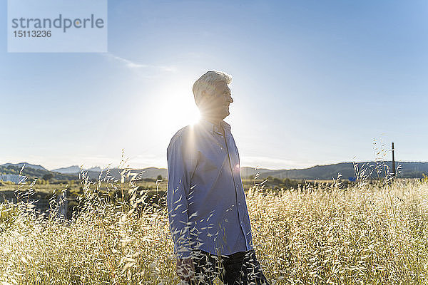 Älterer Mann steht bei Sonnenuntergang auf einem Feld