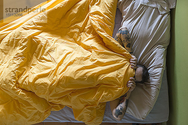 Tätowierter Mann im Bett liegend  Decke über dem Gesicht