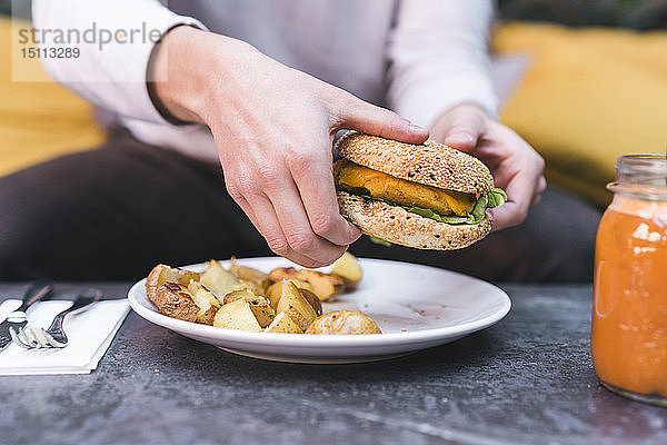 Nahaufnahme eines Mannes  der einen Veganer-Burger mit Kartoffeln zum Mittagessen isst