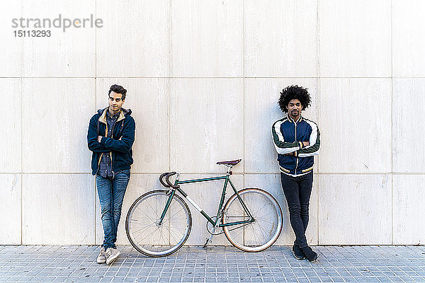 Porträt von zwei Männern mit Fahrrad  die an einer Mauer stehen