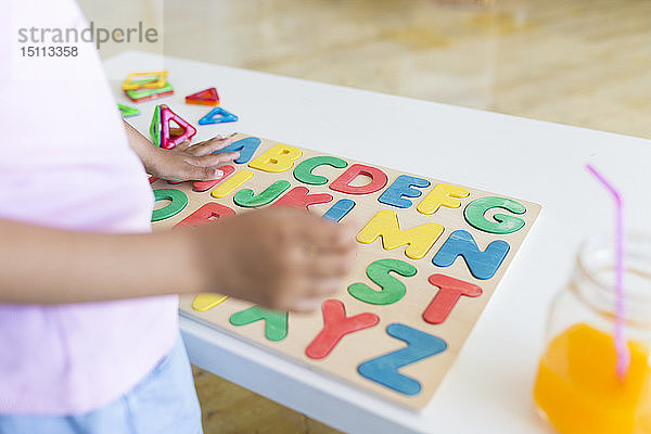 Nahaufnahme eines Mädchens  das mit einem Alphabet-Lernspiel auf dem Tisch spielt