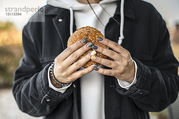 Hände einer jungen Frau mit bemalten Nägeln  die einen Hamburger hält  Nahaufnahme
