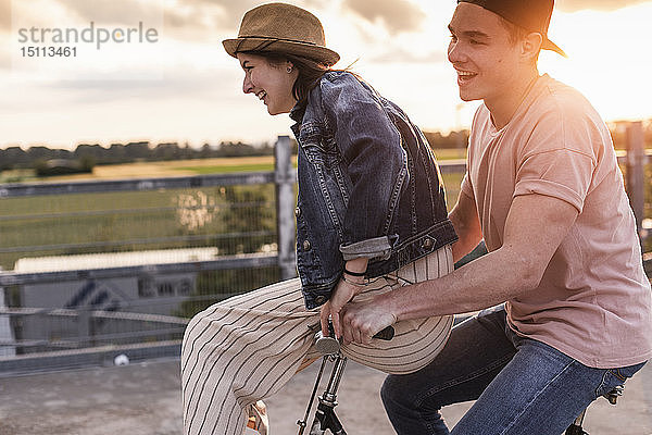 Glückliches junges Paar zusammen auf einem Fahrrad bei Sonnenuntergang auf dem Parkdeck