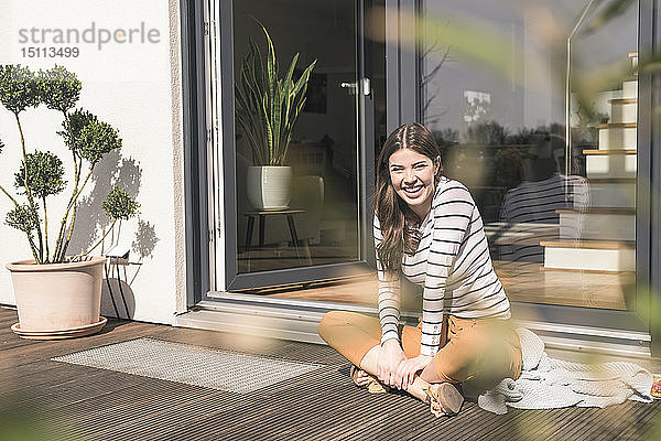 Porträt einer lachenden jungen Frau  die zu Hause auf der Terrasse sitzt