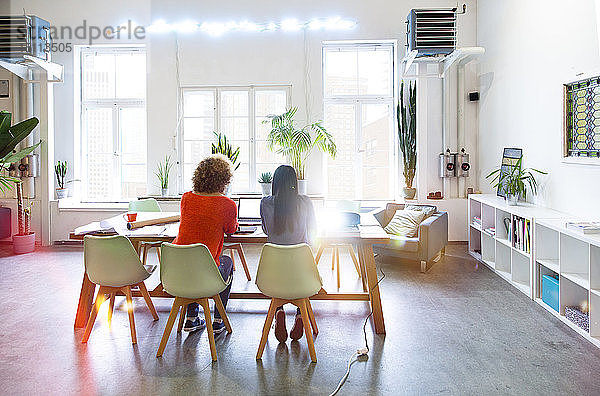 Rückansicht von zwei Frauen  die in einem modernen Büro mit Videoprojektor auf dem Tisch arbeiten