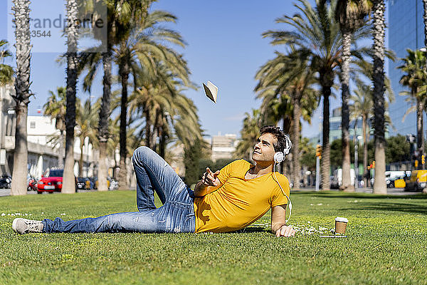 Spanien  Barcelona  auf dem Rasen liegender Mann in der Stadt mit Kopfhörern  der sein Notebook auskotzt