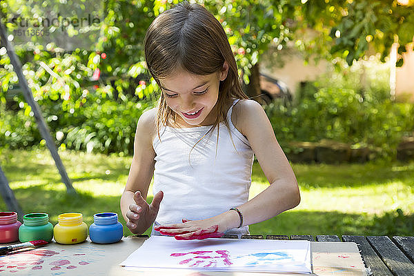 Lächelndes kleines Mädchen  das mit der Hand Farbe auf ein Blatt Papier druckt