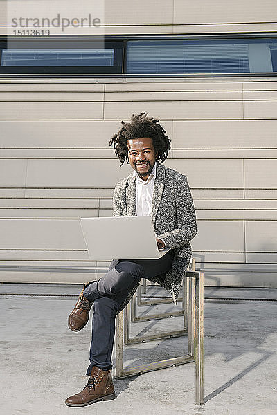 Porträt eines lächelnden Geschäftsmannes auf Fahrradständer vor dem Büro mit Laptop