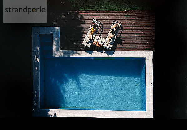 Zwei schöne Frauen sonnen sich auf einer Terrasse neben dem Pool