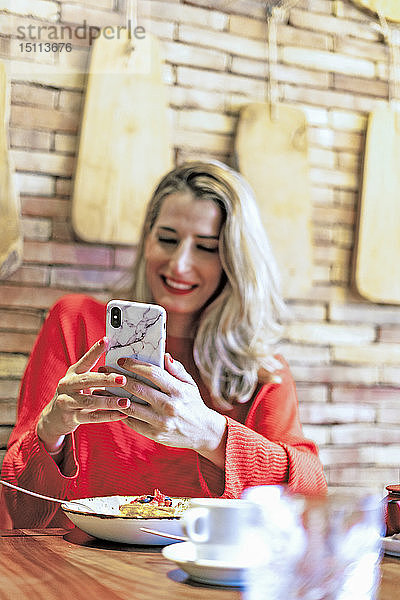 Lächelnde Frau benutzt Mobiltelefon in einem Cafe