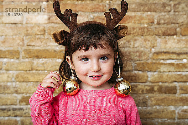 Porträt eines lächelnden Kleinkindes mit Stirnband aus Rentiergeweih und Weihnachtskugeln