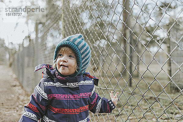 Kleinkind Mädchen in warmer Kleidung an einem Zaun im Wald