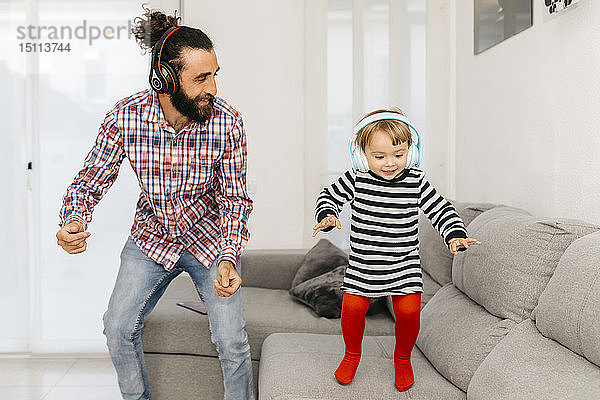 Vater und kleine Tochter tanzen im Wohnzimmer  während sie mit Kopfhörern Musik hören