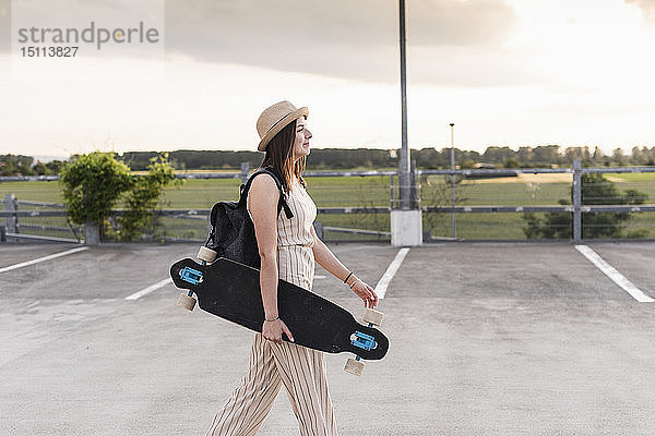 Junge Frau mit Longboard zu Fuss auf dem Parkdeck