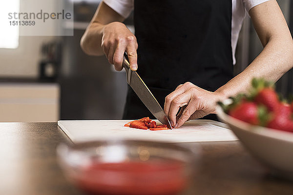 Nahaufnahme einer Frau  die in einer Küche Erdbeeren mit einem Messer schneidet