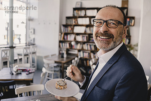 Lächelnder reifer Geschäftsmann bei einem Stück Kuchen in einem Café