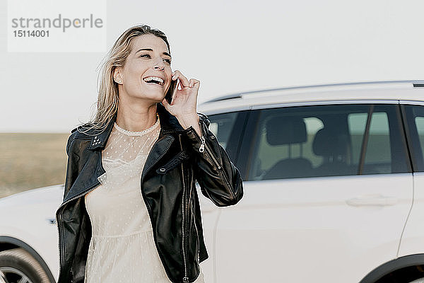 Blonde Frau mit Smartphone  weißes Auto im Hintergrund