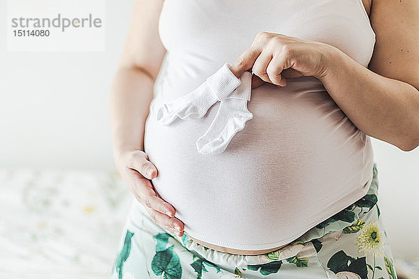 Mittelteil einer schwangeren Frau  die Babysocken hält