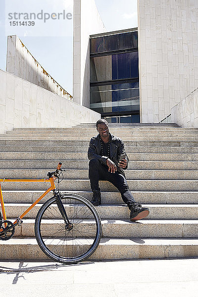 Mann  der ein Selfie macht und auf einer Stufe neben seinem Fahrrad sitzt