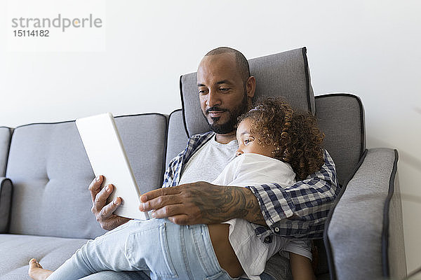 Vater und Tochter sitzen gemeinsam zu Hause auf der Couch und schauen auf die Tablette