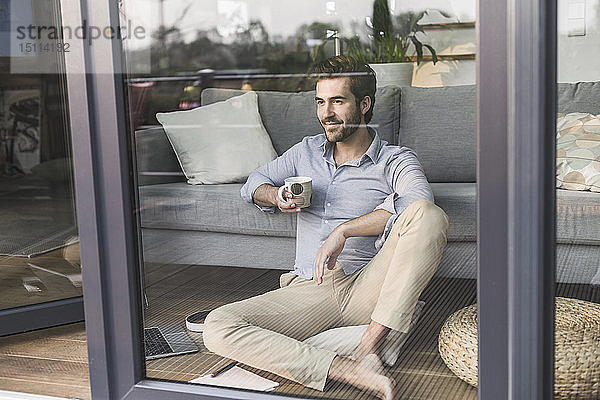 Junger Mann sitzt vor dem Fenster und trinkt Kaffee