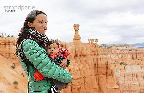 Frau trägt ihre Tochter in einem Tragesitz bei Hoodoos in Bryce Canyon  Utah  USA