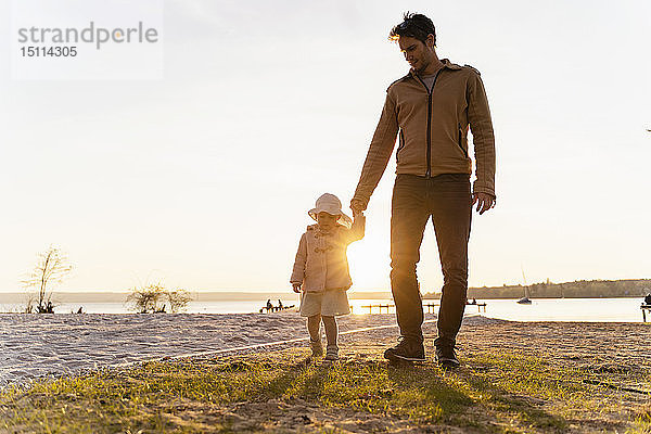 Deutschland  Bayern  Herrsching  Vater und Tochter spazieren bei Sonnenuntergang am Seeufer