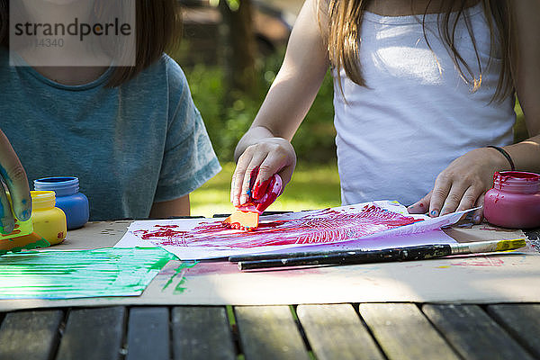 Zwei Mädchen malen bei Tisch im Garten  Teilansicht