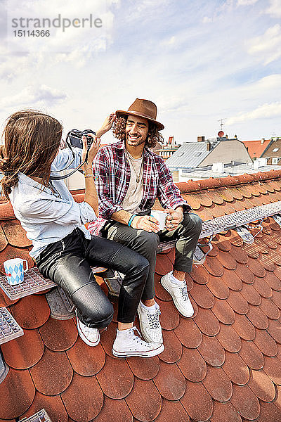 Junges Paar sitzt auf dem Dach und macht ein Foto