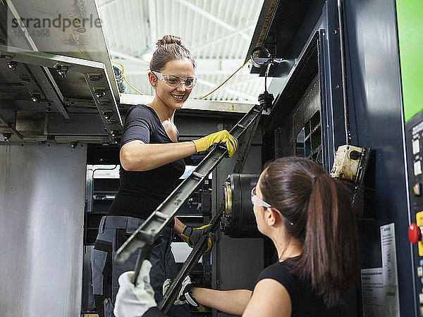 Zwei Frauen arbeiten an einer Maschine. Heben von Stahl