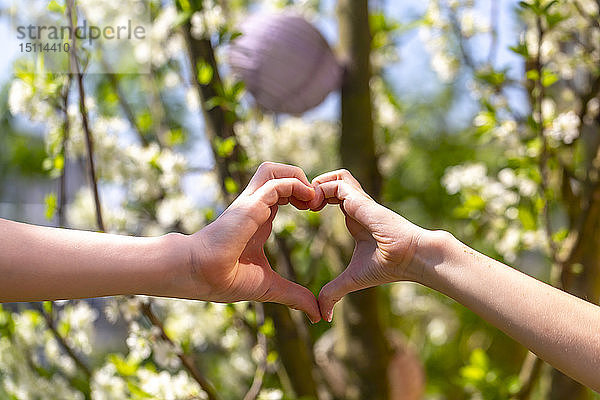 Zwei Kinder formen im Garten mit ihren Händen das Herz