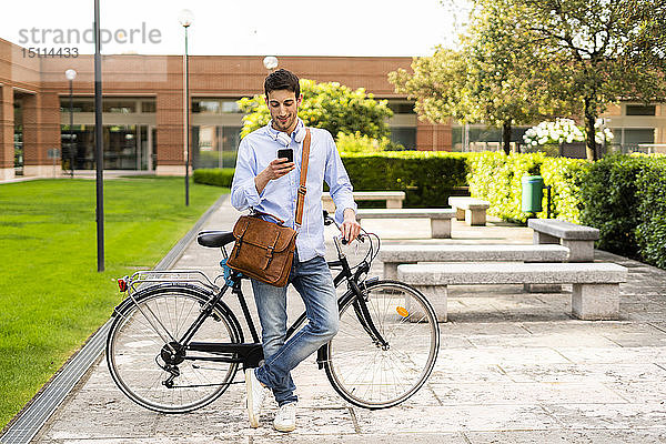 Junger Mann mit Fahrrad und Smartphone  Kopfhörer um den Hals in der Stadt