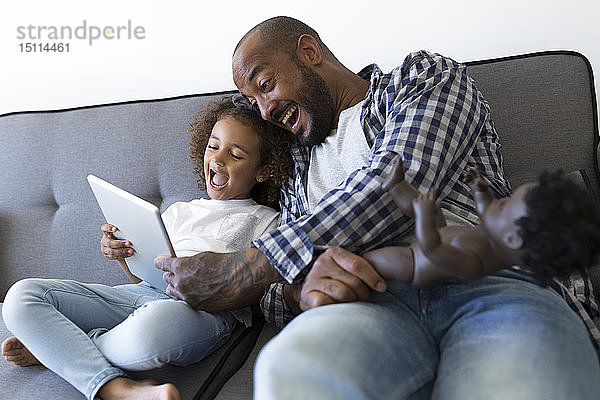 Glücklicher Vater und Tochter sitzen zu Hause auf der Couch und schauen auf die Tablette