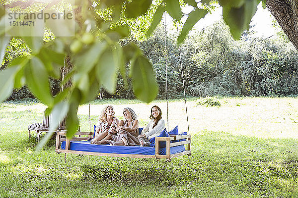 Frauen einer Familie  die sich im Garten entspannen und auf einem Schaukelbett sitzen