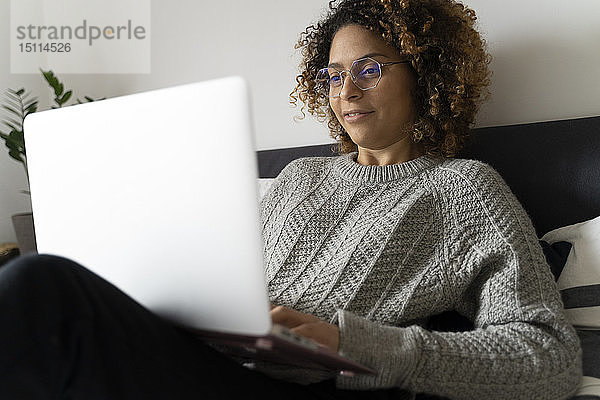 Frau sitzt im Bett  benutzt Laptop  surft im Netz