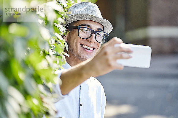 Porträt eines jungen glücklichen Mannes  der mit einer Hecke im Hintergrund Selbsthilfe nimmt