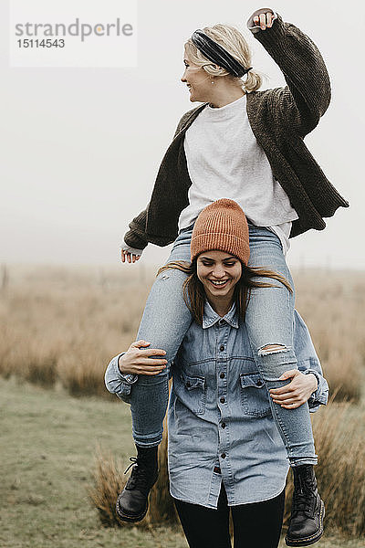 Großbritannien  Schottland  Isle of Skye  glückliche Frau  die ihren Freund huckepack durch die ländliche Landschaft trägt