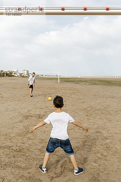 Junge und Mann spielen Fussball am Strand