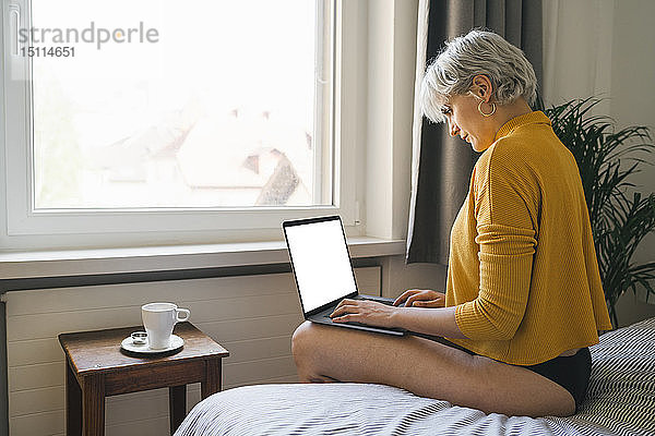 Frau sitzt zu Hause mit Laptop auf dem Bett