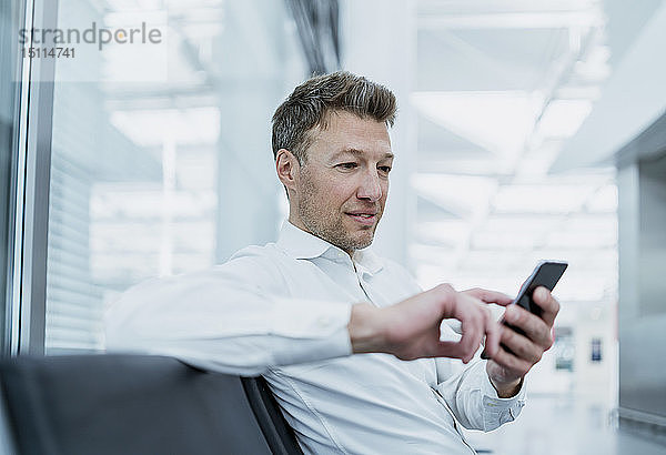 Geschäftsmann sitzt im Wartebereich und benutzt ein Mobiltelefon