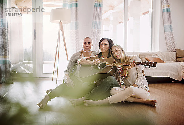 Reife Frau mit zwei Töchtern  die zu Hause auf dem Boden sitzen und Gitarre spielen