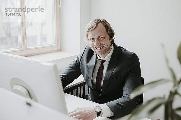 Porträt eines lächelnden Geschäftsmannes mit Computer am Schreibtisch im Büro