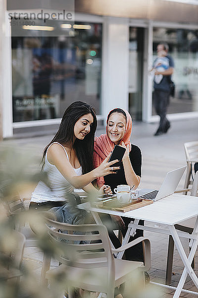 Zwei Freunde sitzen mit dem Handy in einem Straßencafé zusammen