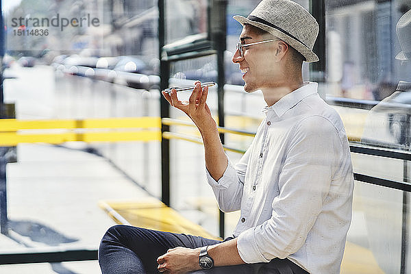 Glücklicher junger Mann benutzt Handy an einer Straßenbahnhaltestelle in der Stadt